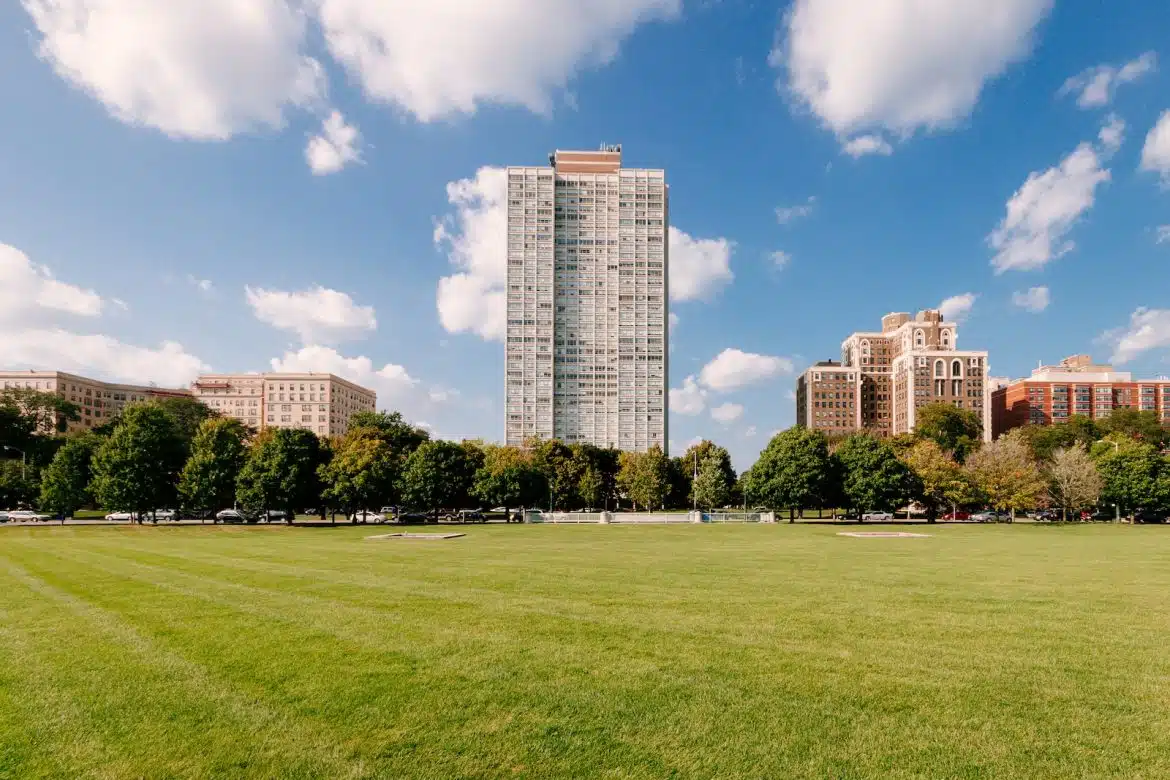 green grass field near city buildings under blue sky during daytime